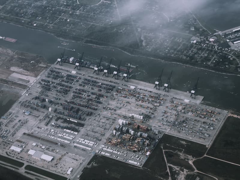 High-level aerial view of a container terminal, showing rows of stacked containers, quay cranes and the surrounding waterway.