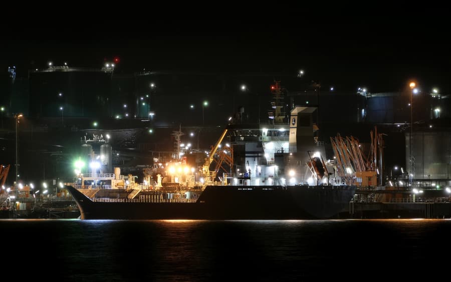 A products terminal at night, with a tanker berthed alongside illuminated storage tanks and loading infrastructure.